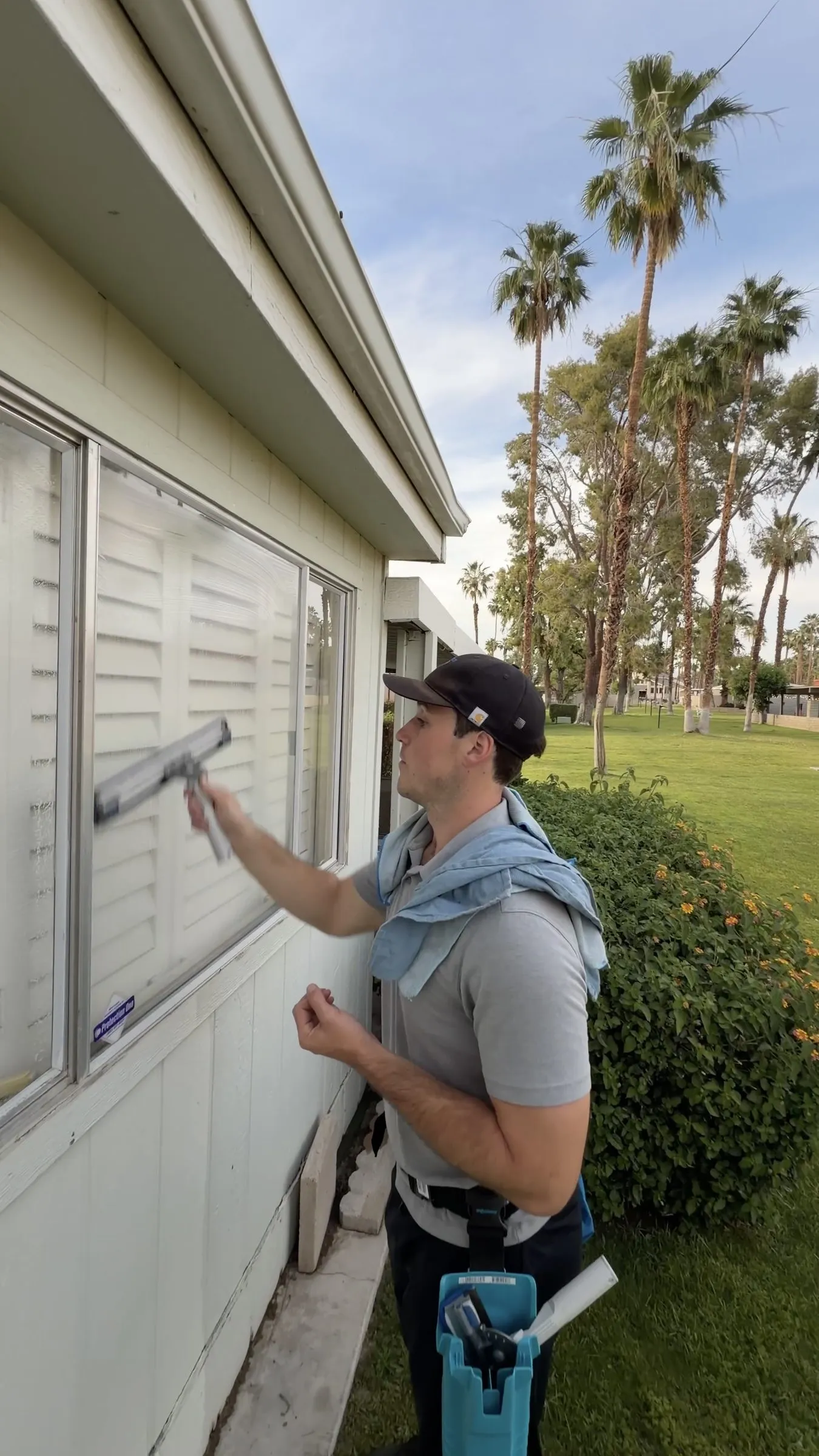 Technician squeegeeing an exterior window, palm trees behind